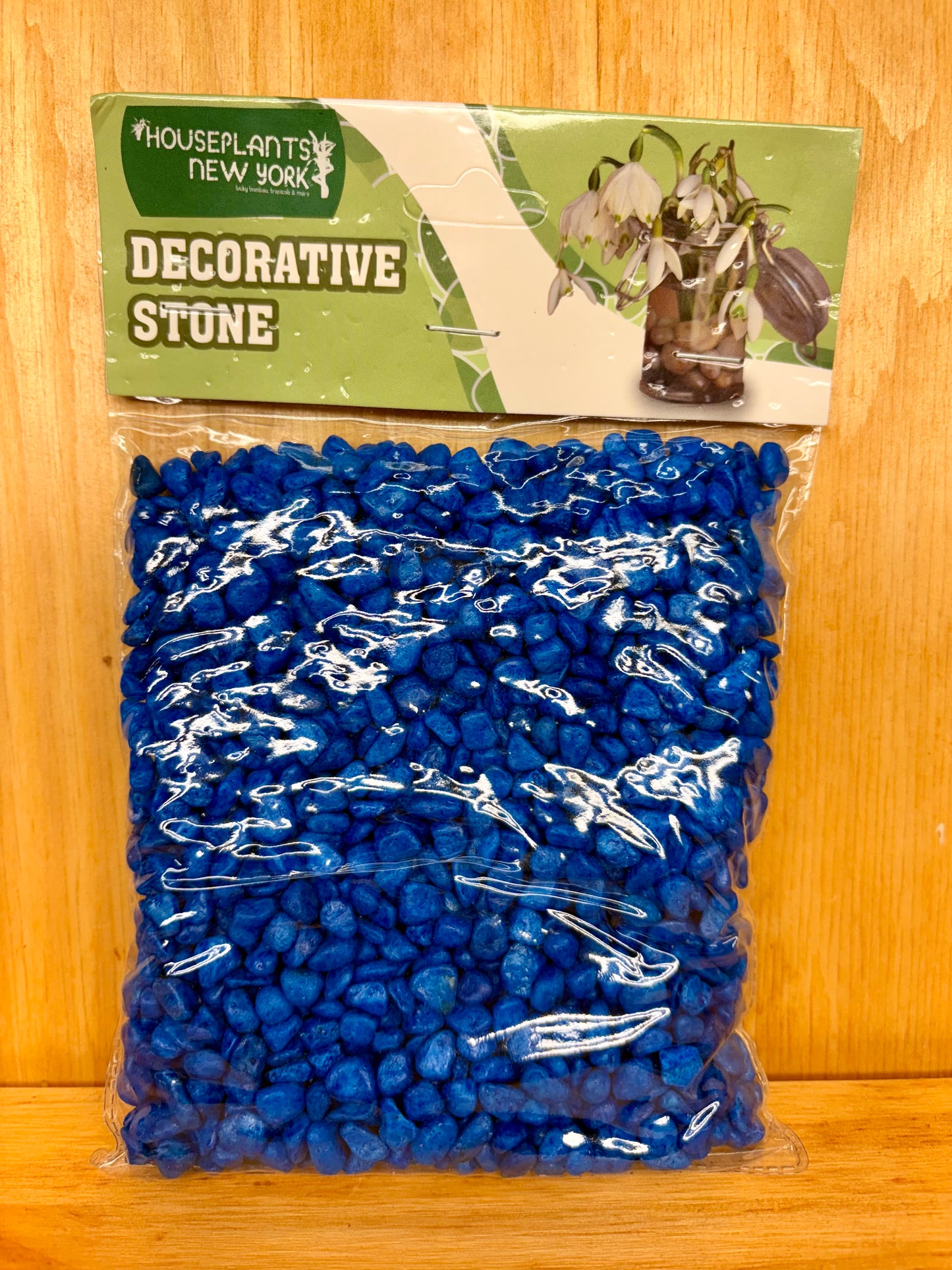 Bag of blue decorative stone with a green label on a wooden surface