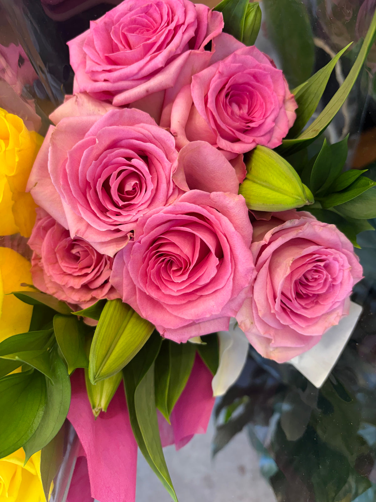 Pink roses with unopened lily buds and green foliage in a wrapped bouquet
