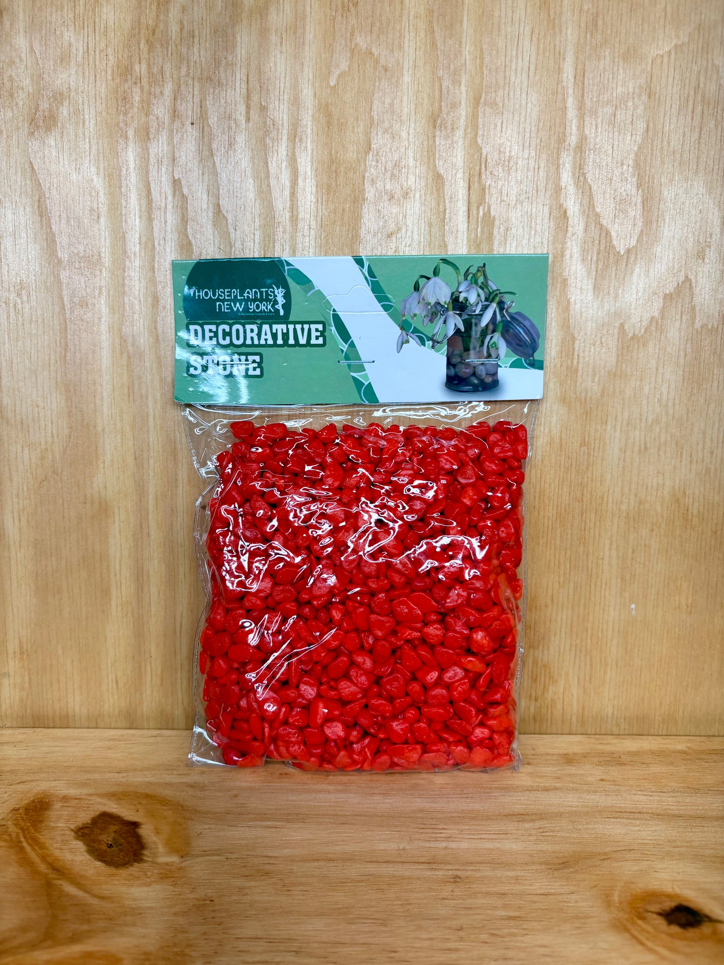 Bag of red decorative stones with a label on a wooden surface