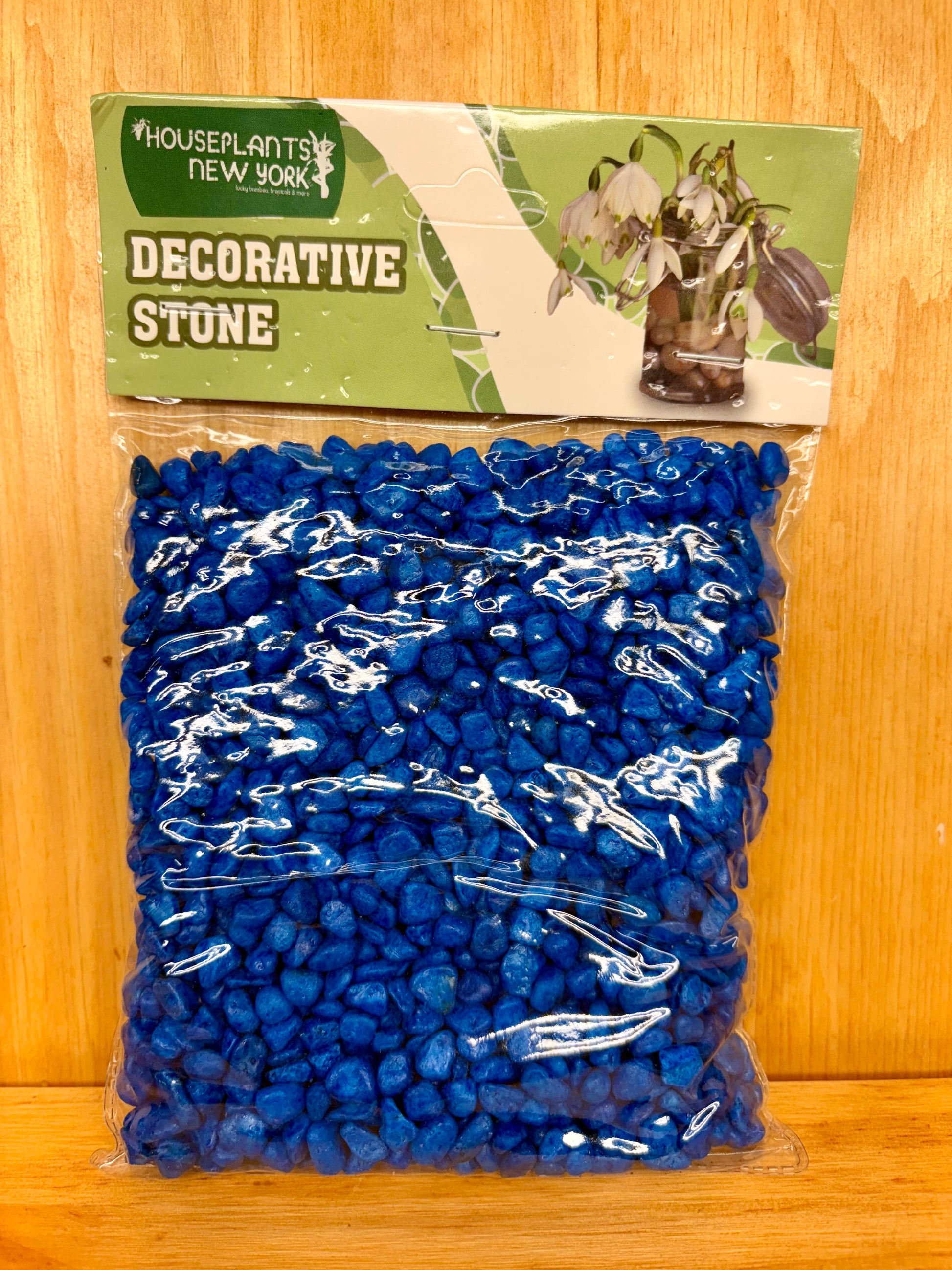 Bag of blue decorative stone with a green label on a wooden surface