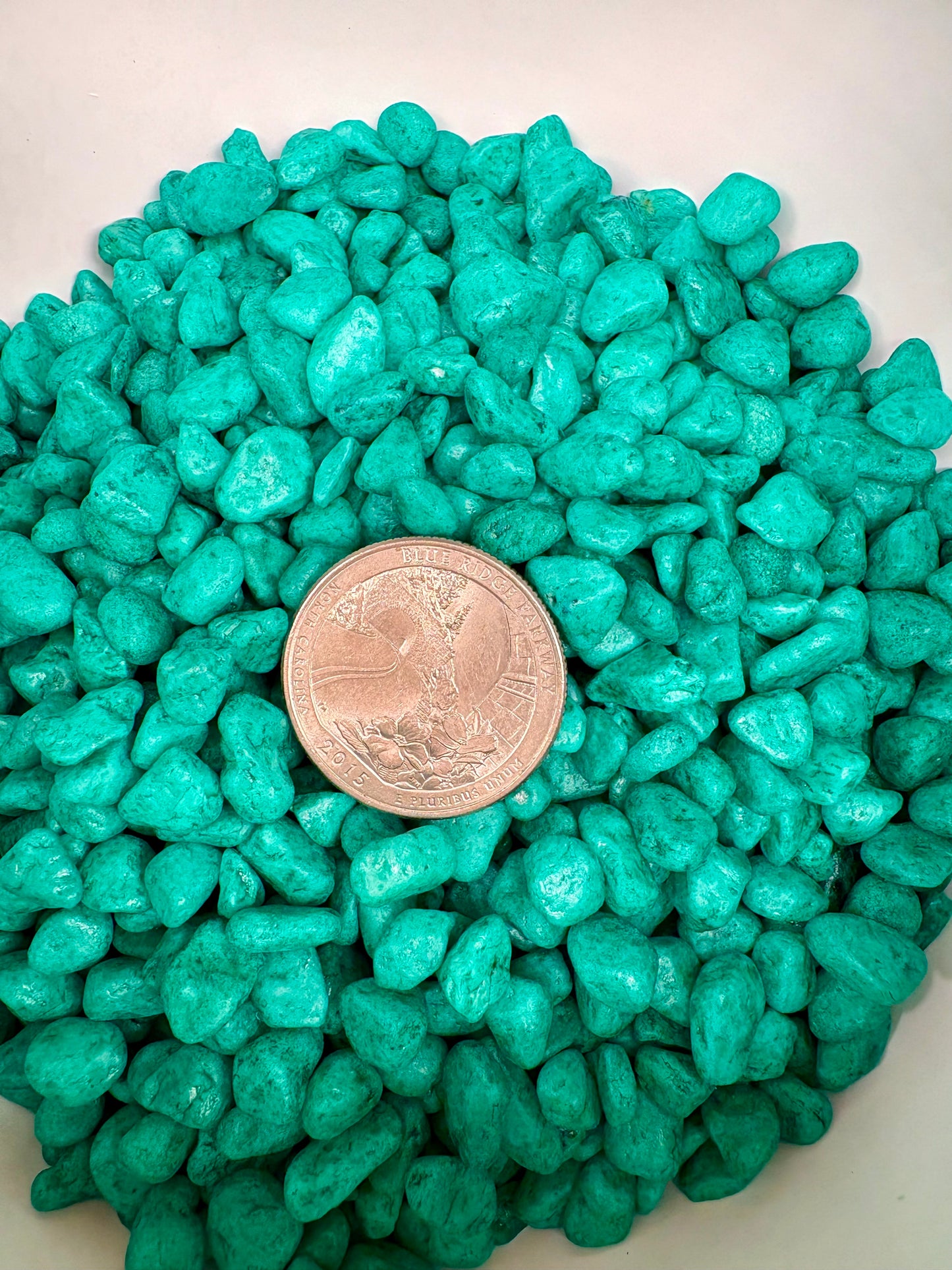 Turquoise stones with a coin for size comparison on a white background
