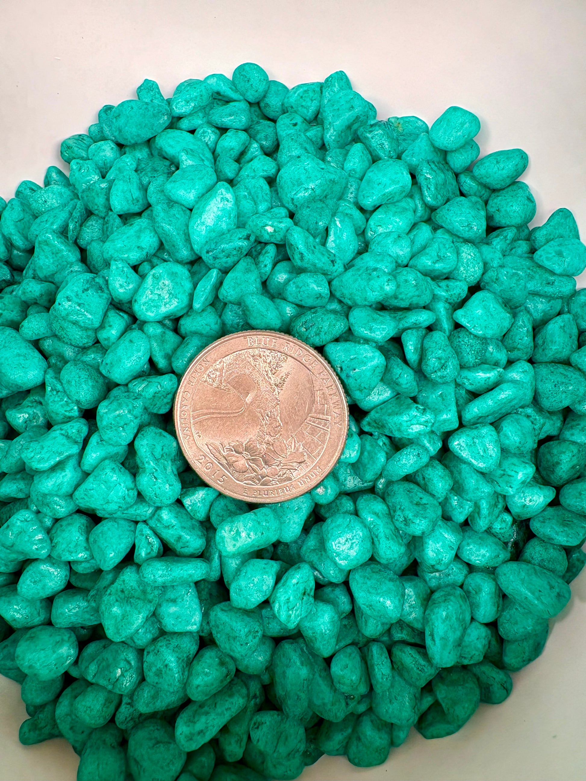 Turquoise stones with a coin for size comparison on a white background